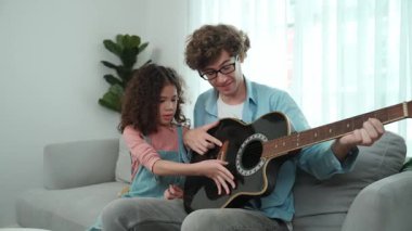 Beyaz bir baba, tatlı kızına koltukta otururken gitar çalmayı öğretiyor. Müzik öğrenirken babasına gitar çalarken bakan tatlı öğrenci kız. Aile eğlence konsepti. Pedagoji.
