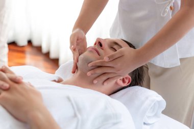 Beyaz adam stres önleyici kafa masajından ve lüks bir tatil beldesi veya otel spa salonundaki modern ışık ortamında yüz güzelliği eğlencelerini şımartmaktan hoşlanıyor. Sessiz.