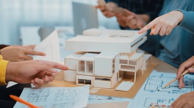 Bir grup mimari tasarım işbirliğine girişerek, modern çalışma alanındaki planlar ve belgeler arasında bir modeli tutkuyla tartışıyor, takım çalışmasını ve yaratıcılığını resmediyor. SACTR