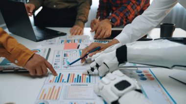 İşbirlikçi bir toplantıda insanlar ve çizelge ve verileri analiz eden bir robot sergileniyor. Çevre, yenilikçi teknolojiyle modern bir çalışma alanını yansıtır. Noogenesis