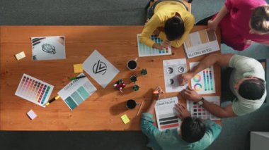 Proje yöneticisi renk paletleri seçerken tasarımcının tablete baktığı yukarıdan aşağıya hava görüntüsü. Profesyonel grafik tasarımının en üst görüntüsü ve logoya bakın. Yetenekli ekip grafikleri seçiyor. Sempozyum.