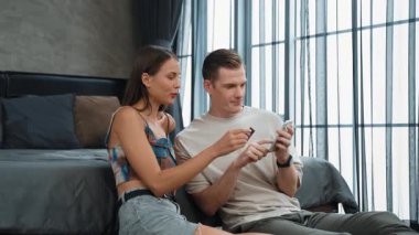 Genç çift, kredi kartıyla ödemek için internet üzerinden ödeme uygulaması ve dijital cüzdan kullanarak yatak odasında oturuyor. Mobil internet üzerinden alışveriş ve modern alımlar. Düzenle