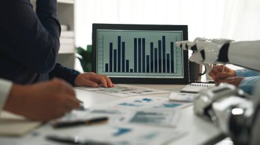 Finansal grafikler, modern teknoloji ve parlak bir ofis ortamında takım çalışmasının yer aldığı profesyonel bir iş toplantısı. Noogenesis