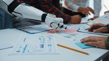 İnsanlar ve bir robot arasındaki işbirliğini gösteren gelecekteki bir ofis sahnesi. Etkili karar verme ve yenilikçi çözümler için grafikler ve verilerin analizi üzerinde duruluyor. Noogenesis