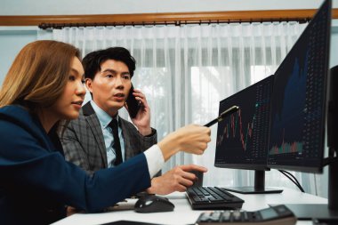 Gülümseyen Asyalı işadamı komisyoncu dinamik borsa veritabanını arıyor. Kadın iş ortağı, iç işyerindeki kar eden uygulama programını karşılaştıran ekranlara işaret ediyor. İnfobahn.