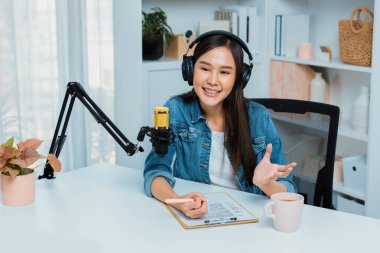 Sosyal medyada kulaklıkla canlı yayın yapan Asyalı sunucu modern stüdyoda yaşam koçluğu veya pazarlama dinleyicilerini selamlıyor. Taktik.