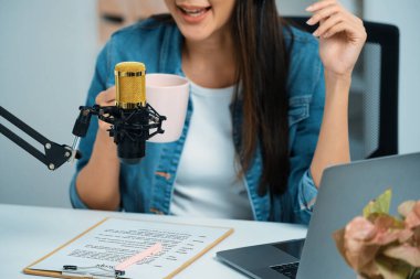 Asyalı sunucu canlı yayında canlı yayında sosyal medyada kulaklık takarak, elinde kahve fincanı tutarak, stüdyoda yaşam koçluğu veya pazarlama yapan dinleyicileri selamlayarak konuşuyor. Taktik.