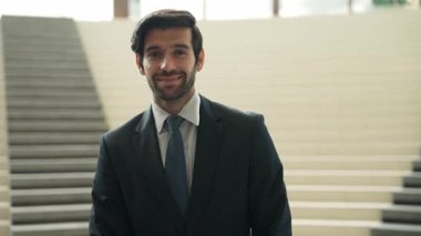 Akıllı iş adamı merdivenlerde kameraya bakıyor. İş elbisesi giyerken kameraya gülümseyen başarılı adamın yakın çekimi. Yönetici, kameraya bak. Hareket eden kamera. Sevinçli..