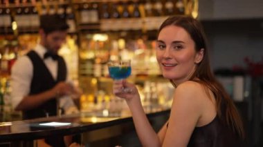 Güzel bayan konuk kameraya bakarak poz veriyor. Kulüpteki akıllı barmen geçmişi ile ilgili toplantı için lüks tezgah barında mavi Hawaii kokteyli ile karışık votka içiyor. Vinosity.