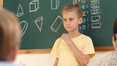 Matematik teorisiyle kara tahtanın önünde duran beyaz çocuk konuşuyor ve fikir sunuyor. Yeni öğrenciye bakarken farklı tatlı öğrenciler oturuyor ve kendini tanıtıyor. Eğitim. Pedagoji.