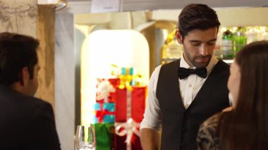 İyi görünümlü barmen hoş geldin içkisi veriyor. İçki tezgahındaki müşterilere dostça sohbetler ediyor. Temiz profesyonel barmen kostümünün içinde harika bir ilk izlenim bırakıyor. Vinosity.