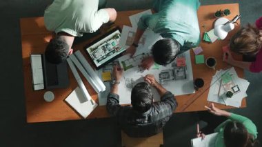 Planı elinde tutan inşaat mühendisi ekibinin en iyi görüntüsü ve dizüstü bilgisayar, proje planı ve planıyla masada duruyor. Yapışkan notları planlayan ve yazan yetenekli proje yöneticisinin havadan görünüşü. Sempozyum.