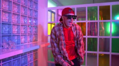 Yakışıklı, beyaz tenli sanatçı kurşun ışıkla dans etmek için dans ediyor. Güneş gözlüklü, şapkalı çılgın hippi dans ediyor ve modern gece kulübünde serbest dans dinlemenin tadını çıkarıyor. Mutluluk.