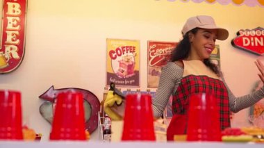 Profesyonel İspanyol restoran işçisi dans ediyor ve yemek barının arkasında duruyor. Kırmızı önlüklü çekici garson kameraya bakarken serbest stil müziğe geçiyor. Çılgın ve komik dans. Mutluluk.