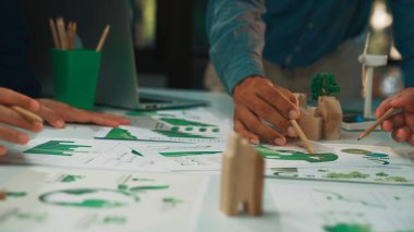 Bu görüntü, sürdürülebilir kalkınma odaklı, çevre dostu tasarım modelleri ve grafikleri sergileyen işbirlikçi bir planlama oturumuna katılan dinamik bir ekip yakalar. SACTR