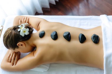 Lüks tatil köyündeki kaplıcalarda sıcak taş masajı. Gün ışığı sükunet ortamında, mutlu kadın müşteri bazalt taş masajından zevk alıyor. Rahatlatıcı bir sıcaklıkla vücudun üzerinde süzülüyor. Sessiz.