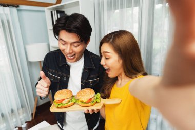 Gülümseyen sunucu şefler akıllı telefonlarıyla fotoğraf çekiyorlar. Özçekim yoluyla. Yemek programında çift hamburger tutuyorlar. İnfobahn.