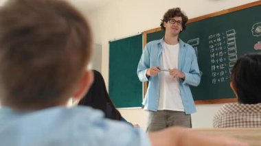 Matematik formülü veya teorisi ile karatahtanın önünde dururken sınıfın etrafına bakan profesyonel akıl hocası. Çeşitli ilköğretim öğrencileri matematik dersinde öğreniyor, çalışıyor ve oturuyor. Pedagoji.