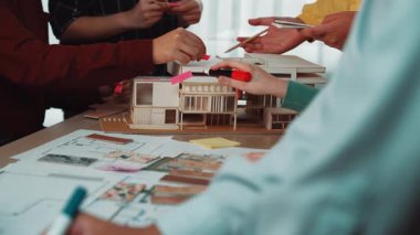 Canlı bir çalışma alanı, mimari modeller, çizimler ve renkli notlar üzerinde işbirliği içinde çalışan çeşitli profesyonellerle bir tasarım oturumu kaydeder. SACTR