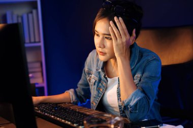 Stresli, genç, güzel Asyalı yaratıcı proje yaratıcısı sosyal medyayı araştırmak için bilgisayara bakıyor ve geceleri daha çok neon modern ofisin planlama kanalı stratejisine ulaşılıyor. Taktik.