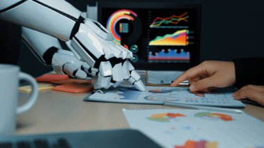 Robotik bir kol insan eliyle veri tablolarının üzerinde etkileşime girer, bu da modern veri analizinde insan ve teknolojinin karışımını işaret eder. Noogenesis