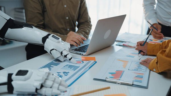 A dynamic business meeting illustrates the synergy between human and robot as they analyze charts and data on a laptop, emphasizing modern workplace innovation.Noogenesis
