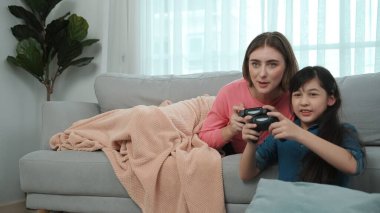 Annem kanepede yatarken, mutlu kız oyun oynuyor ve oturuyor. Beyaz bir ebeveyn ve çekici zeki bir kız elinde joystick ile birlikte vakit geçirip maç kazanmaya odaklanıyor. Yaşam tarzı. Pedagoji.