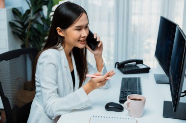 Gülümseyen güzel Asyalı iş kadını akıllı telefondan borsa grafiğini modern ofisteki bilgisayar ekranında analiz etmek için arıyor. Zenginliğe yüksek kazanç sağlama kavramı. Taktik.