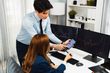 Gülümseyen işadamı cep telefonundaki dinamik borsa verilerini, iç ofisindeki internet sitesi uygulamasını analiz etmek için not yazan kadınlara gösteriyor. İnfobahn.