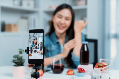 Seçici odaklı akıllı telefon ve gülümseyen genç, güzel Asyalı karışık çilek ve kiraz suyu detoksu değerlendirmesi sosyal medyada sağlıklı ürün tanıtımı sunuyor. Taktik.