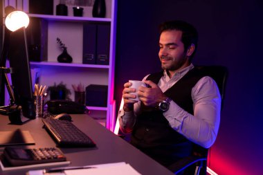 Gülümseyen zeki işadamı, elinde kahve fincanı olan satış ekibiyle buluşuyor ve geceleri Mor Neon Light Home Office 'deki bilgisayar ekranında ürün hedef pazarını araştırıyor. Tahmin et..