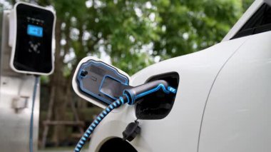 Doğal yeşil araba parkındaki ekolojik temiz enerji şarj istasyonundan gelen fütürist akıllı EV şarj aletinin şarj ettiği elektrikli araba. Alternatif enerji kullanan gelecekçi çevre dostu elektrikli araba. İnceleyin