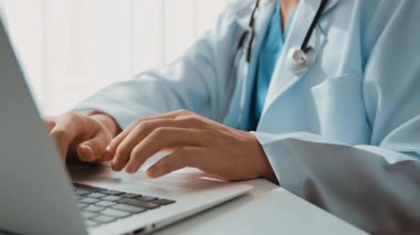 Hastanedeki doktor masasında oturup dizüstü bilgisayar üzerinde çalışıyor. Hasta test sonuçlarını teşhis ediyor, hastalıklar ve hastalıklar için tedavi planı geliştiriyor. Sağlık personeli ve sağlık hizmetleri. Ağır çekim. Katı.