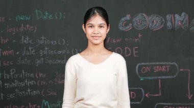 Genç öğrenci başarılı planını kutlarken kolunu kaldırdı. Mühendislik koduyla karatahtaya bakarken kameraya bakan mutlu genç, STEM sınıfında yazılı. Öğretim