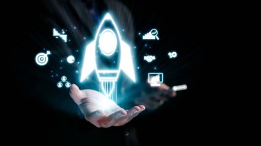 Bir el, çeşitli iş ve teknoloji simgeleri arasında yenilik ve büyümeyi sembolize eden, dijital gelişimin özünü gözler önüne seren parlayan bir roket ikonu sunar. Dörtgen