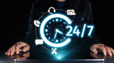 Profesyonel bir figür dizüstü bilgisayarla etkileşime girer, 24 saatlik parlak bir saati iletişim simgeleriyle gösterir, sürekli desteği ve iş dünyasındaki modern bağlantıyı sembolize eder. Dörtgen