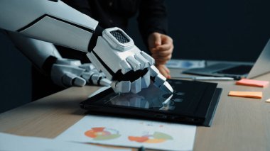 Robotik bir el, bir ofis ortamındaki tablet üzerinde, teknoloji ve iş dünyasının kesişiminin yanı sıra iş ortamlarındaki gelecekteki yenilikleri gösteren dokunmatik bir jest yapar. Noogenesis