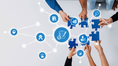 Ellerin iş simgeleriyle çevrili mavi yapboz parçalarını bir araya getirdiği, modern ofis ortamında işbirliğini ve stratejik planlamayı sembolize eden canlı bir takım çalışması. Dostluk