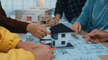 Çeşitli profesyonellerden oluşan bir grup, parlak ve modern bir çalışma alanında ayrıntılı ölçekli bir model ve planları inceleyen bir mimari tasarım projesi üzerinde işbirliği yapmaktadır. SACTR