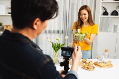 Asyalı güzel kadın yemek uzmanı blog yazarı akıllı kameramanın sosyal medya kavramında canlı yayında kaydettiği canlı yayında salatanın nasıl kolay pişirileceğini öğretiyor. İnfobahn.