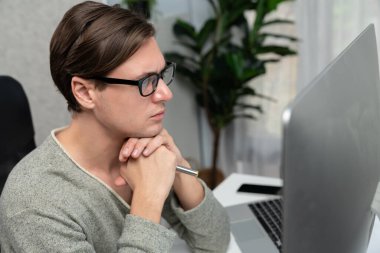 Modern ofiste oturan akıllı bir ofis çalışanı, ciddi bir yüz ifadesi olan, güzel görünümlü gözlük takan bir kamera. Yeni bir profil üzerinde sıradan bir günde çalışan iş adamı kavramı. Bireysel.