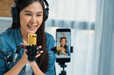 Asyalı sunucu canlı yayında canlı yayında canlı yayında sosyal medyada kulaklık takarak konuşuyor. Dinleyicileri modern stüdyoda koçluk yaparak selamlıyor. Taktik.