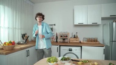 Mutlu baba yemek pişirirken müziğe geçiyor ve modern mutfakta öğle yemeği hazırlıyor. Aktif baba, sebze ve mutfak gereçleri ile çevrili sağlıklı yemek ya da salata yaparken şarkıyla dans ediyor. Pedagoji.