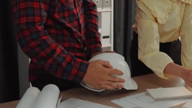 Mimari döküman, ölçüm araçları ve ahşap blokların modern ofiste etrafa saçıldığı masa üzerine planlar yapma konusunda akıllı mimar ve güvenlik mühendisi tartışması. - Yakın çekim. Tanımlama.