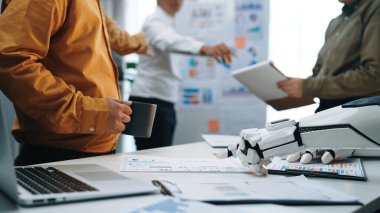 Modern ofis ortamında yenilikçi fikirleri tartışan ve robot araçları kullanan profesyonellerin yer aldığı dinamik bir iş toplantısı. Noogenesis