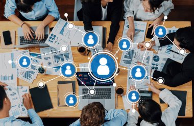 Tahta bir masadaki dijital görseller ve grafiklerle çevrili ve profesyonel etkileşimi gösteren veri analizi ve işbirliği yapan bir ekibin yer aldığı dinamik bir ağ oturumu. Dostluk