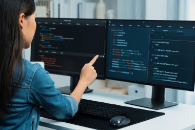 İnternet sitesinde kodlama programı uygulaması olan ve kot gömlek giyen bilgisayar hakkında bilgi veren IT geliştiricisi genç bir Asyalı kız. Güvenlik programlarıyla çevrili iki ekran. Taktik.