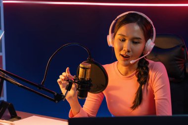 Geceleri podcast 'te olumlu konuşmalar yapan, pembe neon ışıklı modern stüdyoda sunum için dizüstü bilgisayar kullanan, gülümseyen, genç, güzel Asyalı bir etkileyiciydi. Taktik.