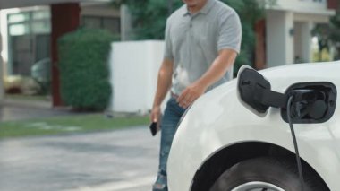 İlerici adam evindeki elektrikli aracın aküsüne emisyonsuz güç bağlantısı kuruyor. Elektrikli araç elektrik istasyonundan EV araba aküsüne kabloyla şarj oluyor.