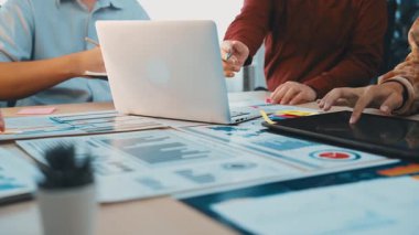 Çeşitli profesyoneller stratejik bir toplantıya katılarak, dijital cihazların bulunduğu canlı bir ofis ortamında mali tablolar ve belgeler analiz ediyorlar. SACTR